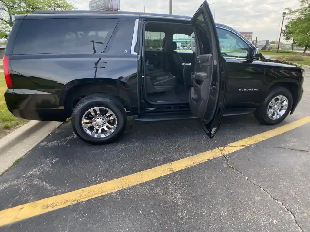 A sleek black Chevrolet Suburban SUV parked on a city street, reflecting light off its glossy finish